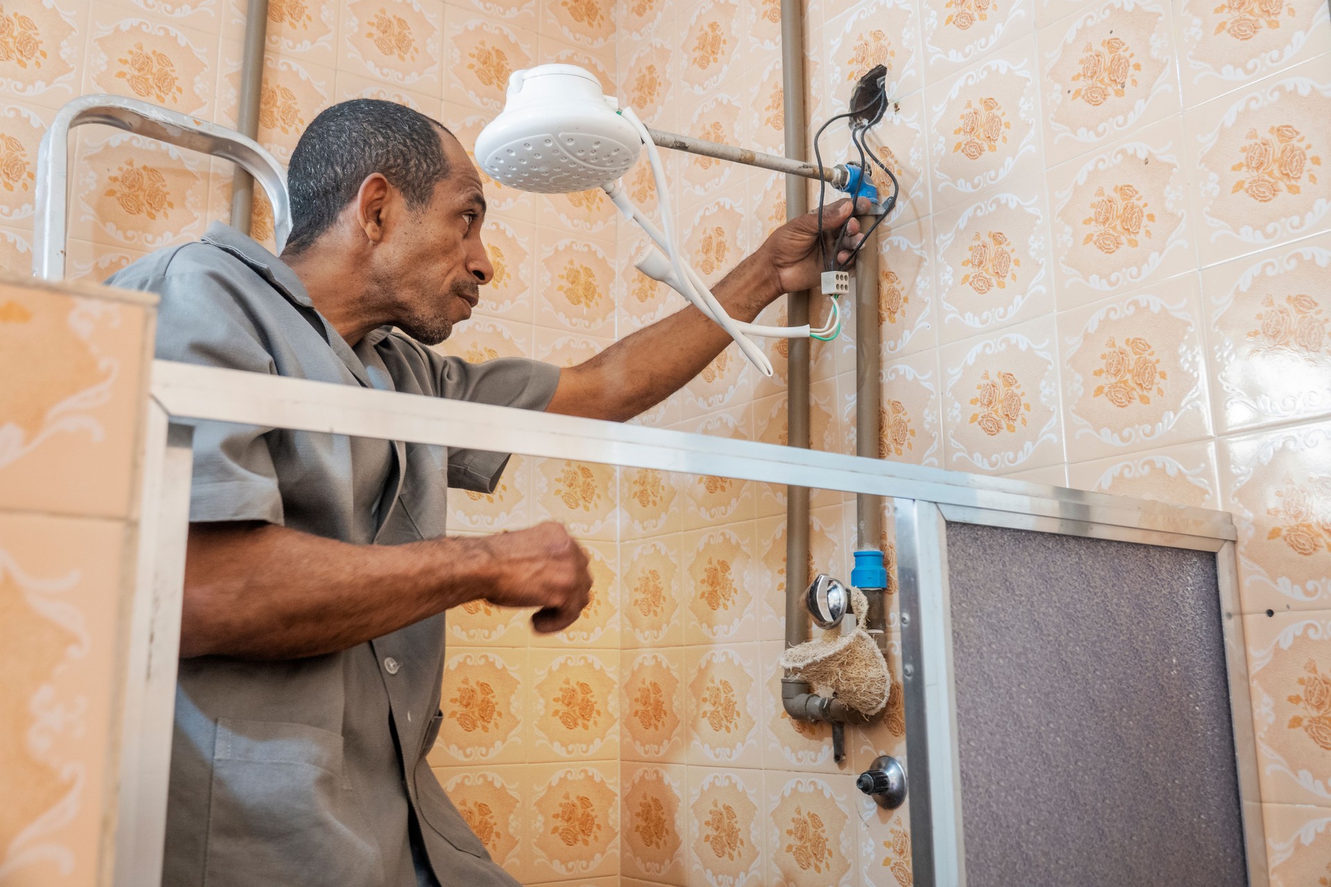 Plumber repairs electric shower in bathroom